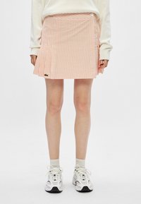 Gestreepte, roze corduroy mini-jurk met een zijknopen sluiting en een geborduurd logo. Draagt met witte sneakers en enkelsokken.