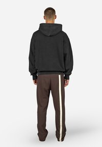 Μαύρη φούτερ με μεγάλο καπέλο και χαμηλούς ώμους, συνδυασμένη με καφέ παντελόνι που έχει λευκή πλευρική ρίγα. Απαλή, άνετη ύφανση.