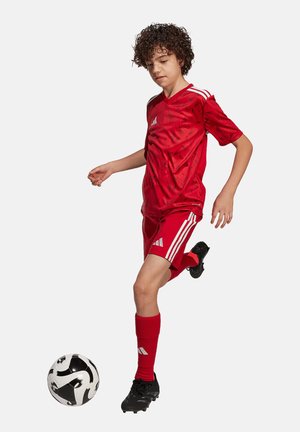 Uniforme da calcio rosso con camicia e pantaloni corti tessurizzati e strisce bianche. Scarpini neri e un pallone da calcio con motivo bianco e nero.