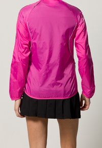 Chaqueta ligera rosa con mangas largas, que presenta una textura suave, un corte ajustado y un ribete reflectante en los hombros y área de la cremallera.