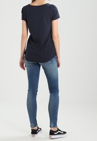 Námořnická modrá tričko s krátkým rukávem a kulatým výstřihem, spárované se světle modrými skinny džíny a černými teniskami. Tričko má volný střih.