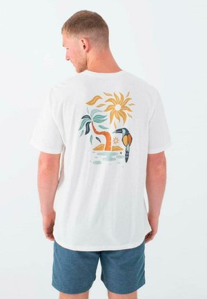 Camiseta de algodón blanca con un gráfico colorido en la parte trasera que presenta un diseño de sol, hojas y un pájaro sobre un fondo claro.