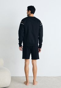 Svart sweatshirt med lange ermer og detaljer; kombinert med svarte shorts. Myk tekstur, avslappet passform, minimalistisk design og uformell stil.
