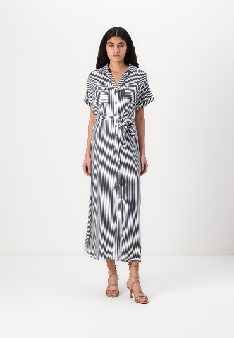 Ριγέ, πουκαμίσα midi φόρεμα σε ναυτικό μπλε και λευκό, με κοντά μανίκια, δύο τσέπες στο στήθος και ζωνάκι, φτιαγμένο από ελαφρύ ύφασμα.