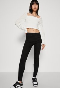 Hvit, kort bluse med teksturert stoff og for brede ermer, kombinert med svarte skinny jeans og svart-hvite joggesko.