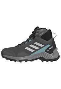 Scarpa da trekking nera e grigia a taglio medio con tomaia in rete, accenti turchesi, tre strisce bianche e suola con trazione robusta. Punta e tallone rinforzati.