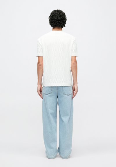 Λευκό πουκάμισο με κοντά μανίκια και υφασμένη υφή, συνδυασμένο με φαρδιά ανοιχτό μπλε τζιν παντελόνια. Η πίσω όψη αναδεικνύει μια άνετη εφαρμογή και casual στυλ.