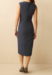 Robe ajustée bleu marine avec un col montant, une fermeture éclair au dos et un ourlet jusqu'au genou ; associée à des escarpins à motif peau de serpent.