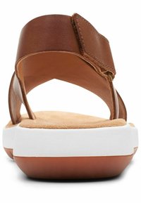 I sandali di pelle marrone presentano una cinghia larga, chiusura in velcro e una soletta imbottita con una suola in gomma bianca e accenti marroni.