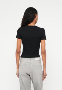 Czarna koszulka z krótkim rękawem o dopasowanym kroju. Tył ma zaokrąglony dekolt i gładką tkaninę. Połączona z jasnoszarymi jeansami.