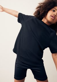 Czarny sportowy t-shirt z krótkim rękawem wykonany z teksturowanej tkaniny, w połączeniu z dopasowanymi szortami. Oba elementy przeznaczone są do aktywności fizycznej.