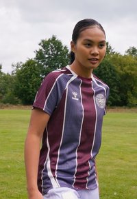 Burgundi ja valgete triipudega spordivorm, lühikeste varrukatega, ringikujulise kaelusega ja logoga vasakul rinnal.