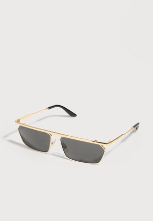 Schlanke rechteckige Sonnenbrille mit schwarzen Gläsern und dünnen goldfarbenen Metallrahmen, die auf einer weißen Oberfläche liegt.