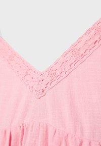 Detailný záber na výstrih ružových šiat s čipkovaným lemom v tvare V a nariaseným detailom pod oblasťou hrudníka.