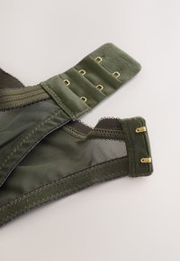 Olivengrøn bh med mesh-stof, guldfarvet hardware, justerbar strop og hægte- og øjeslukning. Har dekorativ blonderkant.