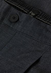 Czarne spodnie materiałowe z subtelnym wzorem w kropki, wyposażone w czarny guzik i etykietę „Flex” blisko pasa. Gładki, teksturowany materiał.