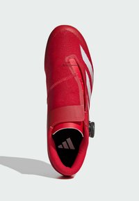 Czerwone buty sportowe z teksturowaną dzianiną na górze, regulowanym paskiem i okrągłym zapięciem na pokrętło. Białe paski akcentujące po bokach.