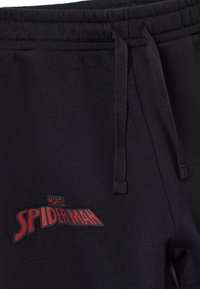 Schwarze Jogginghose mit rotem "SPIDER-MAN"-Logo. Hergestellt aus weichem Material mit elastischem Bund und Kordelzug. Einfaches Design und Textur.