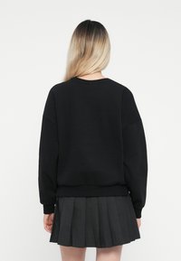 Felpa nera oversize con maniche lunghe, orlo a costine e collo rotondo, abbinata a una gonna plissettata scura. Tessuto morbido; design casual.