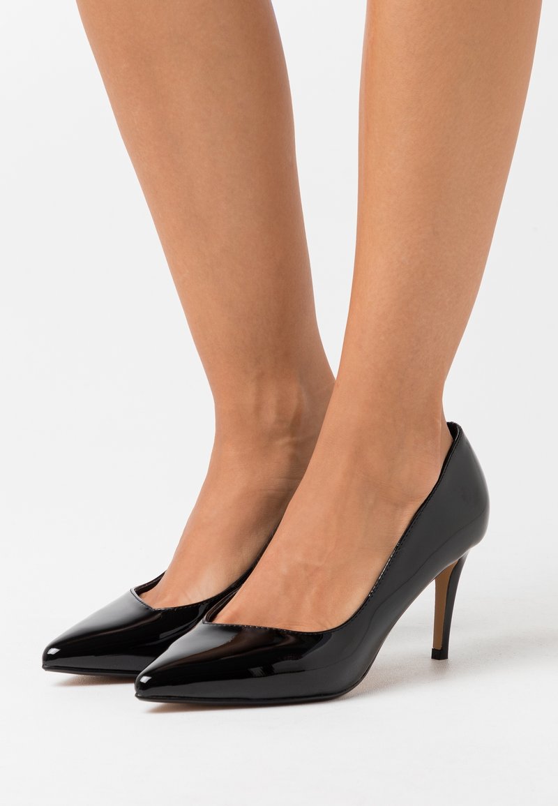 Escarpins en cuir verni noir avec un bout pointu et un talon fin de hauteur moyenne. Le design présente une silhouette élégante et minimaliste sans ornements.