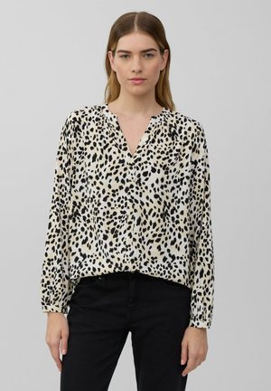 Blouse de couleur claire avec un imprimé léopard noir, col en V et manches longues. Le tissu semble lisse avec une coupe légèrement décontractée. Associée à un pantalon noir.