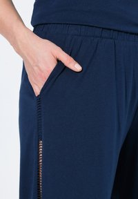 Marineblauwe joggingsbroeken van zacht materiaal, met een elastische tailleband, zijzakken en een decoratieve uitsnijdetail aan de zijkant.