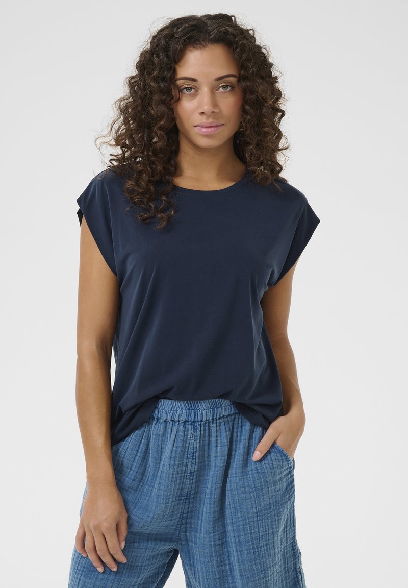 Sötétkék póló rövid, felgöngyölt ujjal és laza szabással, világoskék, texturált, gumis derekú nadrággal párosítva.