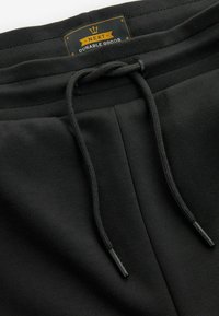 Joggers noirs en matière douce avec une taille élastique, une fermeture à cordon et une étiquette indiquant "NEXT DURABLE GOODS".