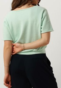 Mint green short-sleeve sweater with a soft texture, relaxed fit, and a wide neckline, paired with dark trousers.