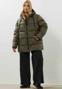 Doudoune vert olive avec capuche, fermeture éclair et poches avant. Présente un design matelassé et des cordons de serrage ajustables sur la capuche.