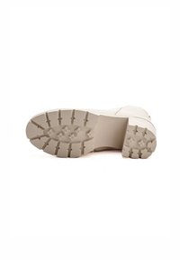 Suela de goma beige con surcos profundos, que presenta una superficie texturizada y un talón reforzado. Diseño de media suela suave y ligeramente elevada.