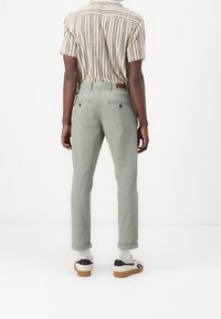 Pantaloni verdi a taglio dritto realizzati in un tessuto strutturato, con tasche posteriori, orli arrotolati e una toppa in pelle marrone in vita.