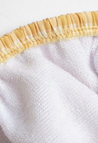 Tessuto di spugna bianco con una morbida texture, bordato in elastico giallo chiaro con dettagli arricciati, caratterizzato da sottili strisce in contrasto.