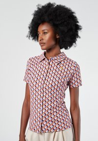 Camicia a maniche corte con bottoni, in un motivo geometrico di rosso, arancio e viola su uno sfondo chiaro; presenta un colletto classico e una texture liscia.