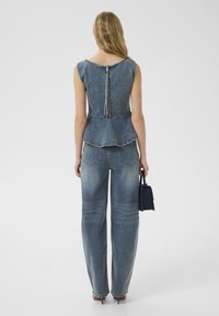 Top in denim a peplum con zip sul retro, abbinato a jeans a gamba larga con scoloriture chiare. Entrambi gli articoli in blu medio con cuciture a contrasto.