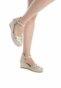 Sandalias de cuña de esparto en color beige con recortes florales, tira en el tobillo, textura tejida y suela de yute natural. Diseño de punta redonda y tacón bajo.