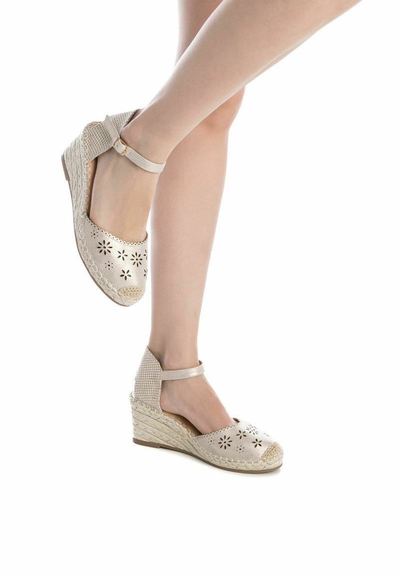 Sandalias de cuña de esparto en color beige con recortes florales, tira en el tobillo, textura tejida y suela de yute natural. Diseño de punta redonda y tacón bajo.