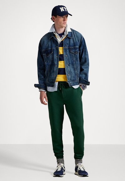 Denimjakke, gul og marineblå stripet skjorte, grønne sweatpants og marineblå caps. Joggesko med hvite aksenter og grå mønstrede sokker.