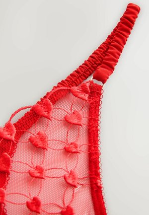 Rotes Bralette aus Mesh und Spitze mit herzförmiger Stickerei, versehen mit einem Rüschenriemen und gewellten Kanten für Textur und Detail.