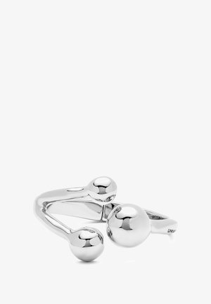 Anillo de metal plateado que presenta un diseño suave y curvado con tres acentos esféricos de diferentes tamaños dispuestos de manera asimétrica.