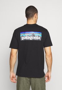 Fekete pamut póló színes hegy grafikai mintával és "patagonia" logóval a hátsó részen. Rövid ujjú és laza szabású.