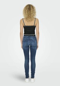 Kék farmer skinny nadrág sima textúrával, öt zsebes dizájnnal és közepes derékkal, párosítva egy fekete, rövid fazonú toppal, amely nyitott szövésű.