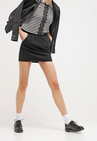 Černá džínová mini sukně s bočními kapsami, v kombinaci s černou koženou bundou a pruhovaným topem s krajkovými detaily. Vzhled doplňují černé šněrovací boty.