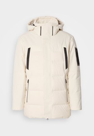 Chaqueta acolchada blanca con un cuello alto, acentos negros en los laterales, bolsillos con cremallera y una textura suave. Diseño de paneles cosidos en toda la prenda.
