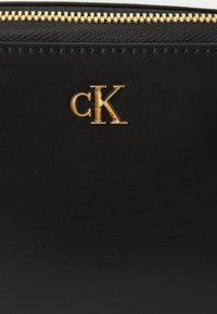 Schwarze Lederbrieftasche mit strukturiertem Finish, ausgestattet mit einem goldenen Reißverschluss und einem goldenen "cK"-Logo auf der Vorderseite.