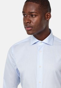 Camisa de rayas azul claro hecha de algodón, con un cuello button-down y un diseño ajustado, con dos botones visibles en la tapeta.