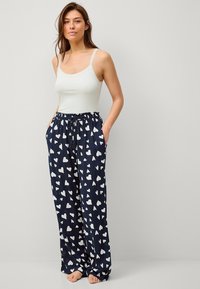 Top blanco sin mangas con encaje, combinado con pantalones de pijama azul marino que presentan un patrón de corazones blancos y una cinturilla elástica con cordón.