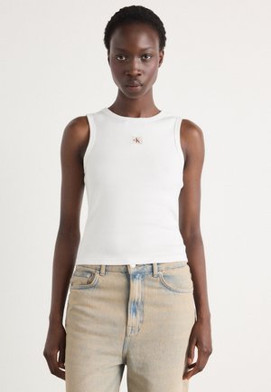 Hvid ribbet tanktop med et lille CK-logo, parret med lyseblå jeans med en falmet tekstur og høj talje.