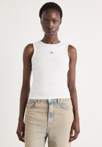 Top a righe bianco con un piccolo etichetta CK, abbinato a jeans azzurri chiari caratterizzati da una texture sbiadita e una vestibilità alta.