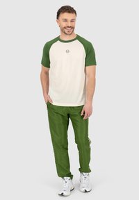 Ensemble de vêtements de sport pour hommes comprenant un haut à manches courtes crème avec des manches raglan vertes et un pantalon vert assorti avec des détails sur les côtés.
